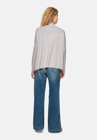 Hellgraues, oversized Oberteil mit hohem Kragen, kombiniert mit blauen, weiten Jeans, die an der Saumkante mit Strassakzenten verziert sind.