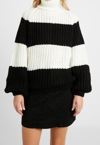 Czarno-biały sweter w paski z dzianiny z golfem, w luźnym kroju i o teksturowanej tkaninie, w połączeniu z czarną spódnicą.