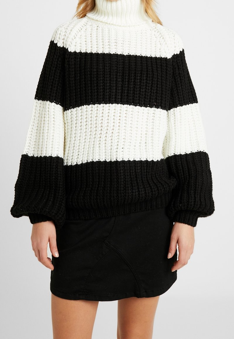 Czarno-biały sweter w paski z dzianiny z golfem, w luźnym kroju i o teksturowanej tkaninie, w połączeniu z czarną spódnicą.