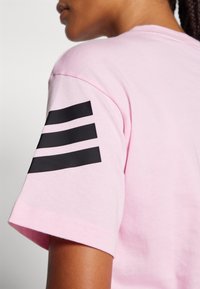 Lyserød kortærmet t-shirt lavet af bomuld, med tre sorte striber på venstre ærme. Glat tekstur med en afslappet pasform.