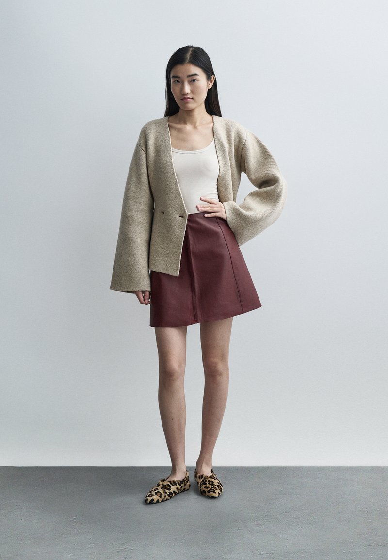 Beige uldcardigan med brede ærmer, lagdelt over en cremefarvet tanktop; kombineret med en burgunderrød lædernederdel og leopardmønstrede sko.