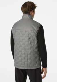 Grau gepolsterte Weste mit einem gesteppten Muster, hohem Kragen und glatter Oberfläche. Über einem schwarzen Langarmshirt getragen, ohne sichtbare Beschläge.