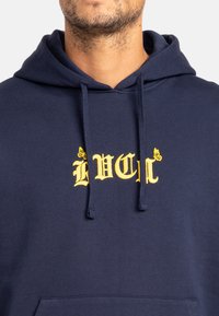 Navy blue hoodie with a kangaroo pocket, featuring yellow embroidered text "LVL" and butterfly accents. Soft cotton fabric and adjustable drawstrings.