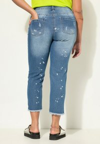 Capris de mezclilla azul claro con manchas desgastadas y dobladillos deshilachados, con bolsillos traseros y cintura de altura media.