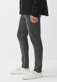 Černá fleecová bunda, šedé slim-fit džíny a bílé tenisky. Džíny mají mírné vyblednutí a standardní pětikapsový design.