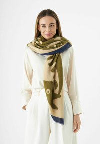 Écharpe en laine pr�ésentant un motif de poisson vert sur un fond beige, avec une bordure bleu foncé, drapée autour du cou. Texture douce.