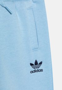 Svetlo modri trenirke iz mehkega blaga, ki imajo stranske žepe in črno vezeno Adidasovo logo na levi stegnu.