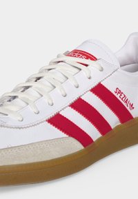 Λευκό παπούτσι Adidas με κόκκινες ρίγες και κείμενο "Spezial", άσπρα κορδόνια και σόλα χρώματος καουτσούκ.