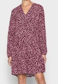 Robe bordeaux à manches longues et décolleté en V, ornée d'un motif floral rose. Coupe ample avec un ourlet à volants, fabriquée à partir d'un tissu léger.