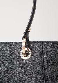 Borsa nera texture con una tracolla nera liscia e un emblema circolare dorato con la scritta "GUESS" incisa.