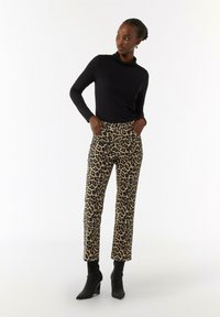 Black long-sleeve top paired with high-waisted, leopard-print trousers. Trousers feature a straight leg design and pockets. Black ankle boots complete the outfit.