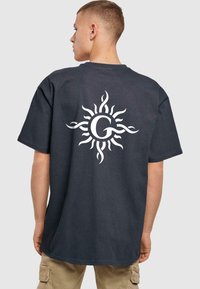 Mørk grå kortærmet T-shirt med et stort hvidt solgrafik og et bogstav 'G' i midten af ryggen. Blødt bomuldsstof.