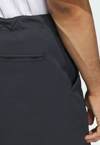 Dunkelgraue Stoffshorts mit einem elastischen Bund, einer Gesäßtasche und kontrastierenden türkisfarbenen Nähten. Glatte Textur und modern geschnitten.