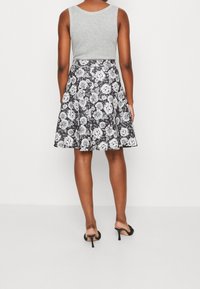 Grå ärmlös topp matchad med en svart kjol med ett vitt blommönster, som vidgar sig vid nederkanten, bärs med svarta sandaletter med remmar.