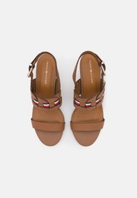 Braune Leder-Slingback-Sandalen mit flacher Sohle, ausgestattet mit einem geflochtenen Riemen in Rot, Weiß und Blau sowie einer metallischen Schnalle.
