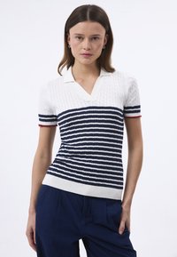 Polo à manches courtes rayé blanc et marine, avec une texture en tricot à câble et un accent rouge au niveau de l'ourlet des manches. Fond côtelé et col ouvert.