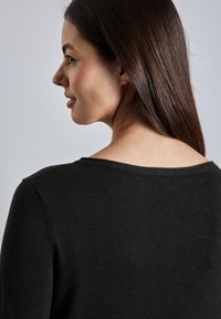 Pull en maille noir avec un large col, des manches longues et une texture douce. Vue de l'arrière, montrant la zone du cou et des épaules.