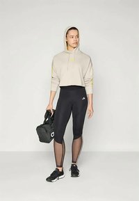 Λιτή μπεζ φούτερ με κορδόνια και κίτρινες λεπτομέρειες, μαύρα κολάν με πλέξεων, μαύρα αθλητικά παπούτσια και μια μαύρη σάκα.