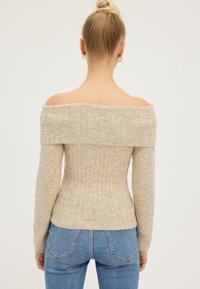 Lichtbeige off-the-shoulder rib gebreide trui met lange mouwen, aansluitend ontwerp en zachte textuur. Gecombineerd met blauwe high-waisted jeans.