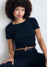 Navy blue ribbed knit t-shirt with short sleeves, knotted at the front, paired with matching leggings featuring a logo tab on the waistband.