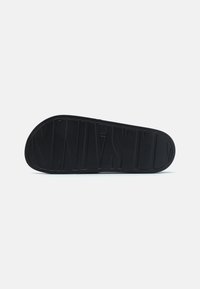 Semelle en caoutchouc noir avec un motif de grip texturé et un nom de marque en relief. Forme arrondie avec un bord lisse, conçue pour l'adhérence et la durabilité.
