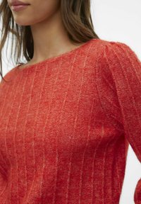 Rød strikket sweater med ribbet tekstur og bred halsudskæring, der har lodrette striber. Blødt stof med en let løs pasform.