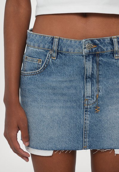 Fustă mini din denim în albastru deschis, cu tiv desfăcut. Are bucle pentru curea, un buton în față și cusături contrastante. Include buzunare frontale.