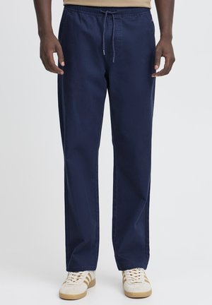 Navy blue cotton trousers with an elastic waistband and drawstring. Straight-leg design, smooth texture, and side pockets. Paired with beige sneakers.