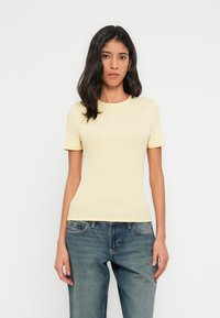 T-shirt à manches courtes côtelée en jaune doux. Coupe ajustée avec encolure ronde. Associée à un jean bleu à coupe décontractée. Texture lisse.
