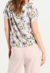 Bloemrijke blouse in lichte stof; heeft roze, gele en grijze bloemen; korte mouwen; ontspannen pasvorm; bevat plooidetails op de schouders.
