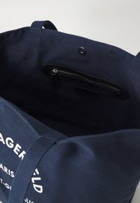 Marineblauwe katoenen tote bag met een ritsvak aan de binnenkant en een logo-opdruk. De tas heeft stevige handvatten en een ontspannen, ongestructureerde vorm.