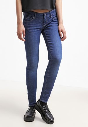 Jean ajustados en denim azul oscuro, con un clásico diseño de cinco bolsillos y costuras sutiles. Combinados con zapatos negros perforados.
