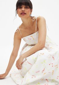 Vestido floral blanco con tirantes ajustables, que presenta coloridos patrones botánicos en todo el diseño y una textura de tela suave y fluida.