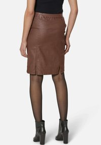 Brauner Leder-Bleistiftrock mit taillierter Passform, Rückenschlitzen und gesteppten Details. Tragen mit schwarzen Stiefeletten und transparenten Strumpfhosen.