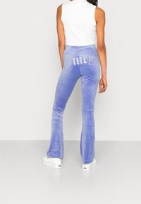 Sammet flarebyxor i ljuslila med "Juicy" i rhinestones på baksidan, tillsammans med vita platåskor.