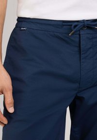 Pantaloni corti blu navy realizzati in tessuto leggero, con una vita elasticizzata dotata di cordoncino e una piccola etichetta con logo sul lato.