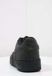 Černé tenisky Nike Air s hladkým koženým svrškem, polstrovaným límcem a strukturovanou gumovou podrážkou s označením na patě.