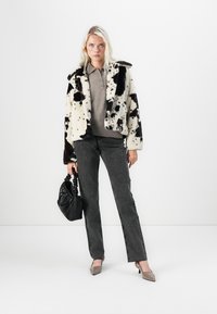 Kunstpelzjacke mit schwarz-weißer Kuhmuster, graues Poloshirt, schwarze Jeans und beige Absätze. Schwarze Handtasche mit Raffung.
