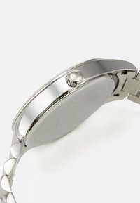 Silver stainless steel watch with a rounded case, textured crown, and a sleek band featuring a unique link design.