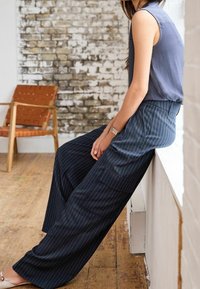 Marineblauwe pinstripe wijde broek met een gestuctuurde afwerking, gecombineerd met een mouwloos grijs topje. Heeft een zijzak en een losse pasvorm.