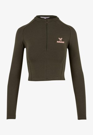 Haut cropped à manches longues en tissu vert foncé, avec un col montant et une fermeture éclair à l'avant. Logo "Delicious" en rose clair sur la zone gauche de la poitrine.