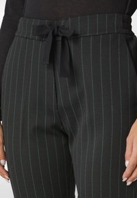 Zwarte op maat gemaakte broeken met verticale groene strepen, uitgerust met een gestrikt tailleband, zijzakken en een gladde stofstructuur.
