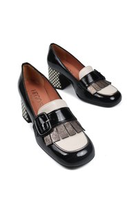 Czarno-białe damskie buty na słupku z klamrą, z frędzlami i metalicznym detalem z przodu oraz obcasem w wzór houndstooth, na białym tle.