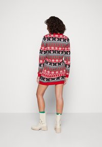 Abito maglione a righe rosse e nere con motivi di fiocchi di neve e polsini a contrasto, abbinato a stivali beige con tacco grosso.
