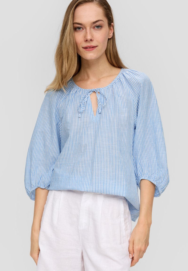 Hellbluse mit Streifen, rundem Ausschnitt und Bindedetail, mit Puffärmeln und lässigem Schnitt. Getragen mit weißen Leinenhosen.