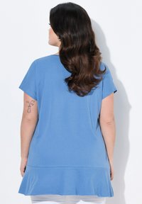 Túnica corta de manga corta en color azul, confeccionada con una tela suave, que presenta un dobladillo acampanado y un corte holgado. Textura suave y diseño sencillo.