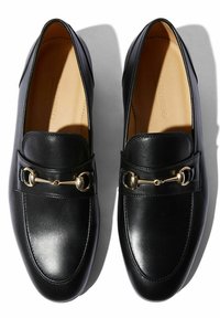 Mocassini in pelle nera con punta rotonda, dettagli in catena dorata sul davanti e superficie liscia, con tacco basso.