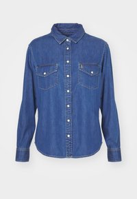 Blue denim button-up shirt with long sleeves, two chest pockets with white snap buttons, and a classic collar.
