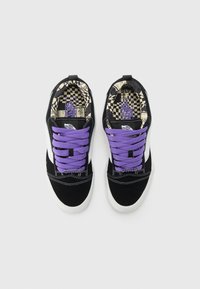 Sneaker in suede nera con lacci viola, suole bianche e una fodera interna a motivo caratterizzata da disegni a scacchi e dal logo Vans.