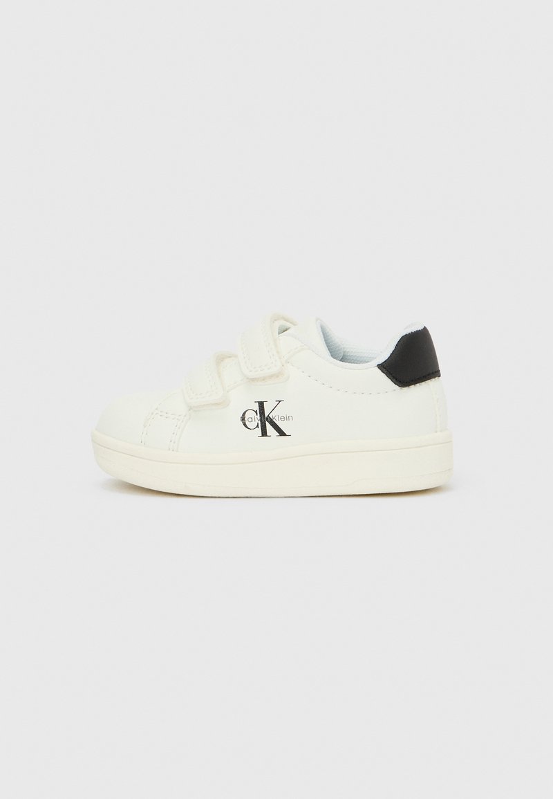 Bela otroška superga z dvema ježkoma, črnim jezičkom na peti in logotipom Calvin Klein na strani, prikazana na enostavni podlagi.